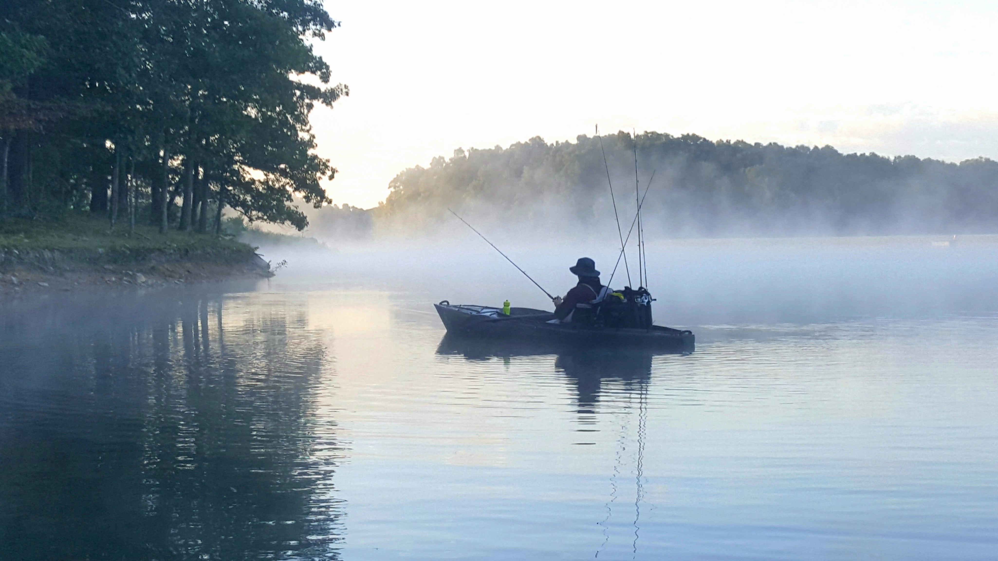 Man fishing out of his kayak while fog rises off the water's surface