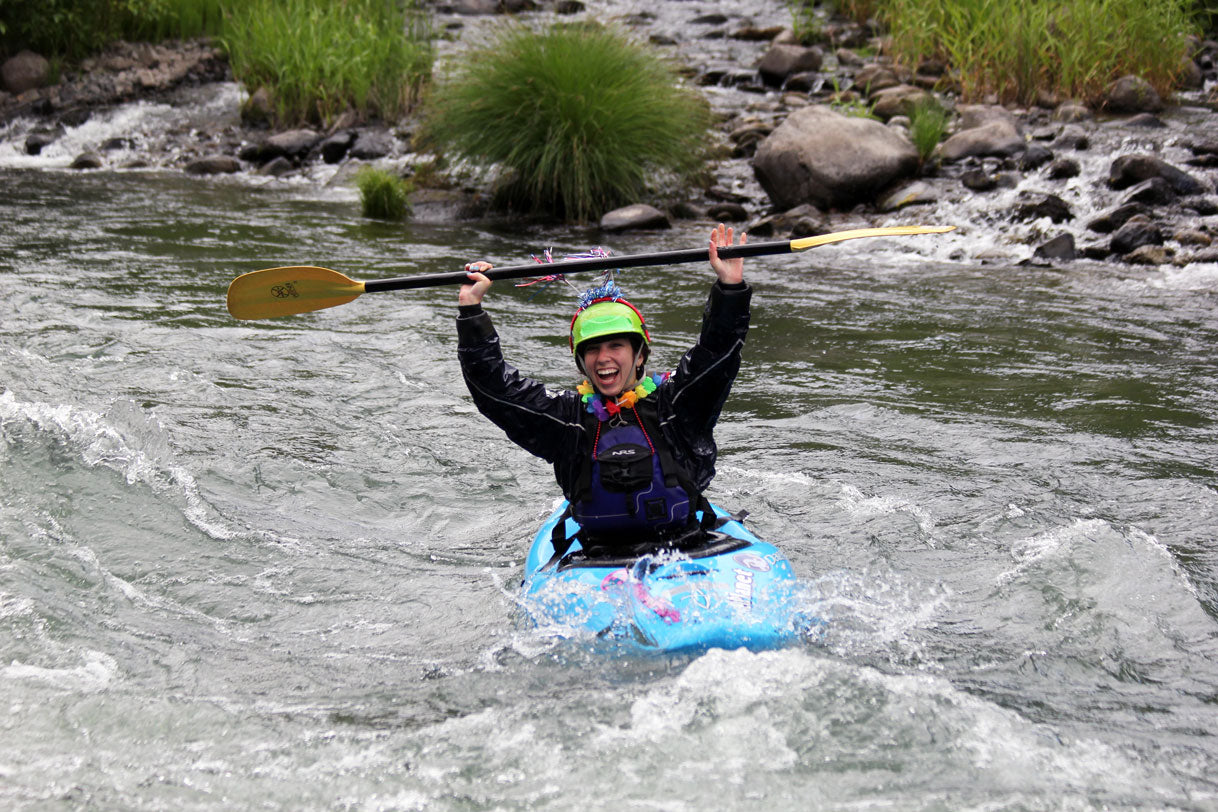 A whitewater kayaker raising their paddle over their head celebrating in the river