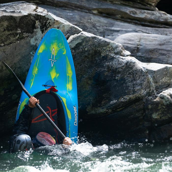 Kayaker performing a stern squirt nose stall on a rock