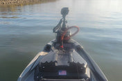 A first-person view from the bow of a fishing boat on a calm body of water, showing a Garmin fish finder screen, mounted camera, and boat equipment under a clear blue sky.