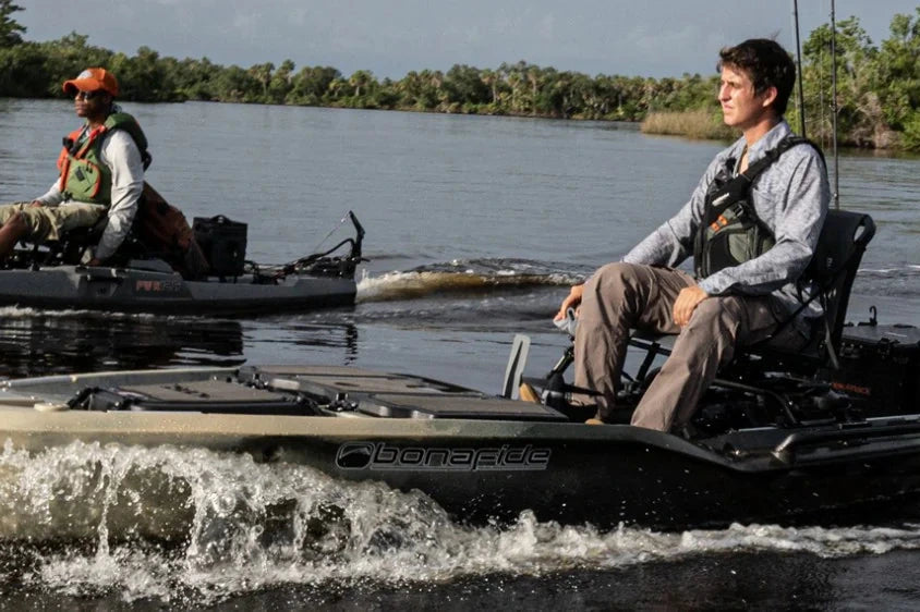 Two people sit in motorized all-terrain boats on calm water, with trees and poles in the background.